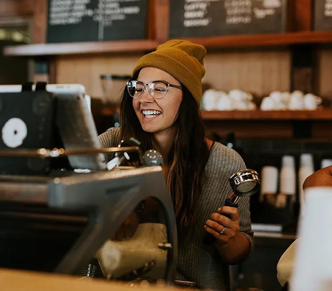 Étudiante souriante travaillant derrière le comptoir d’un café.